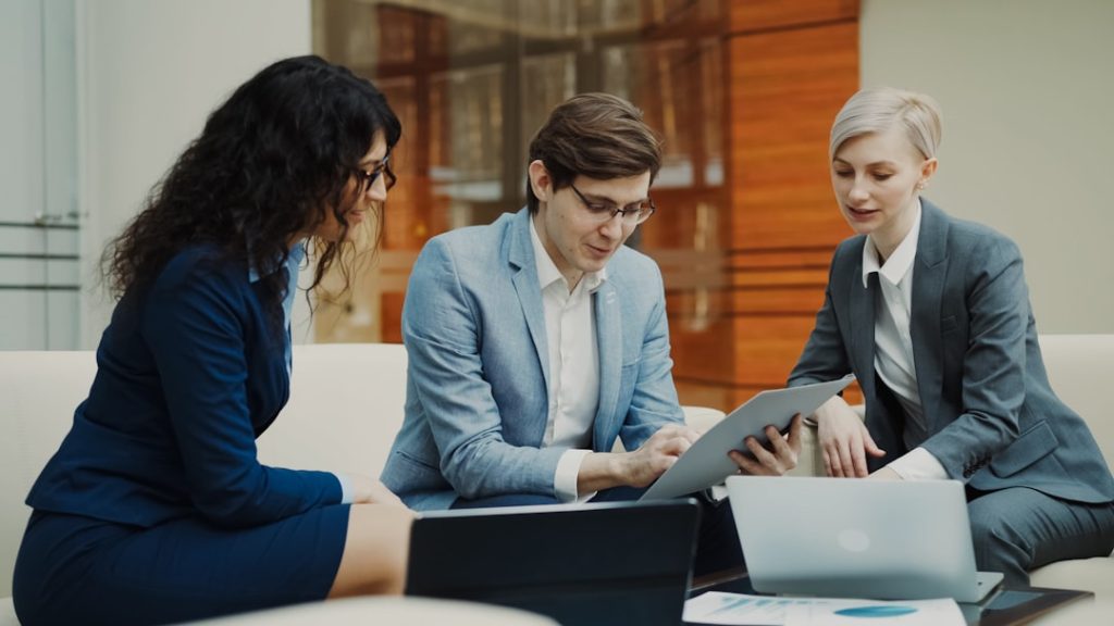 Businessman talking and duscussing future contract with female business partners sitting on couch in meeting room indoors